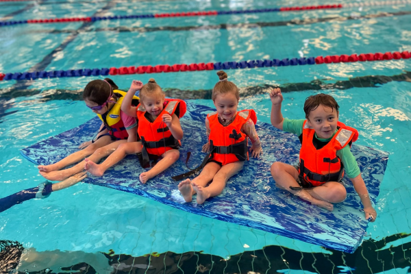Children in life jackets floating on a pool mat