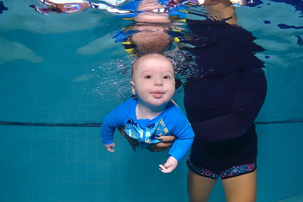An infant boy submerged underwater with the guidance of an instructor